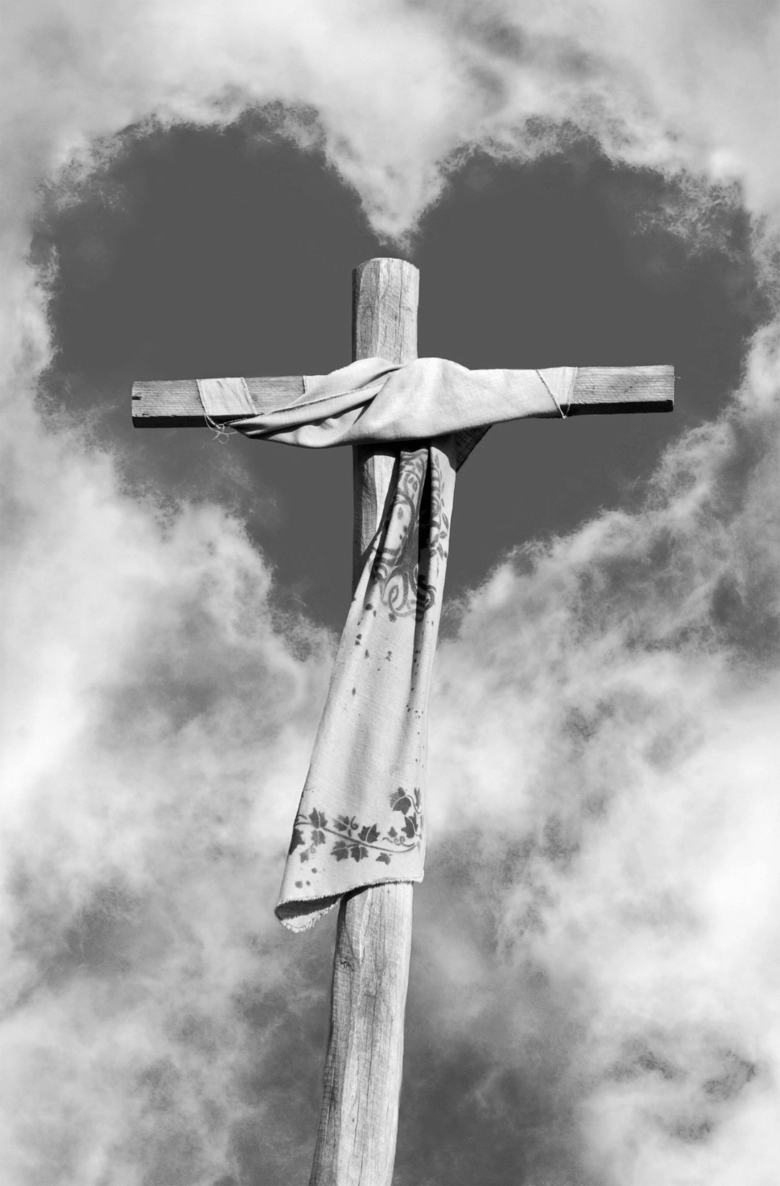 A wooden cross with a draped scarf set against a dramatic cloudy sky, forming a heart shape.