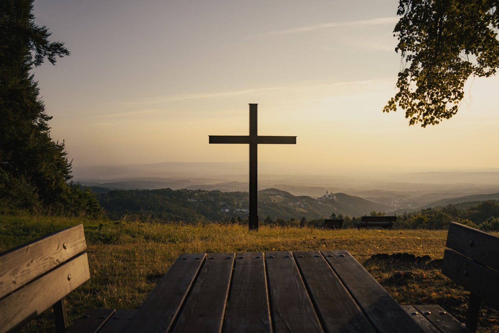 Peaceful Austrian hilltop with a cross at sunset, offering a serene view over the landscape.