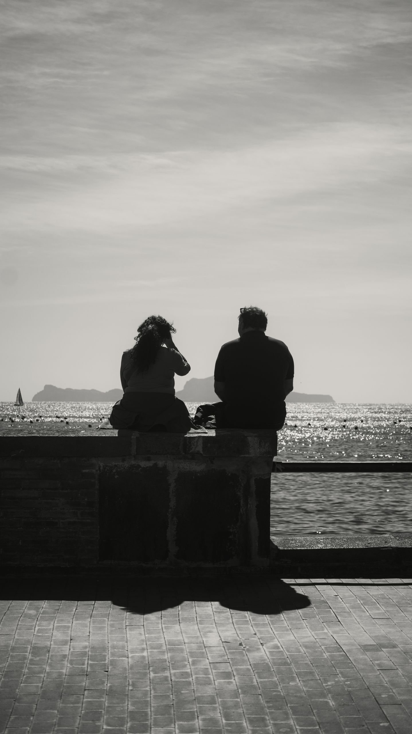 Silhouetted couple enjoys serene view of the sea from a coastal wall, evoking a sense of tranquility.